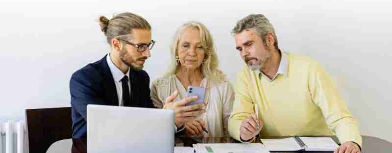 Three individuals collaborating on financial documents during a business meeting., tags: markt für versicherungsplattformen - pexel